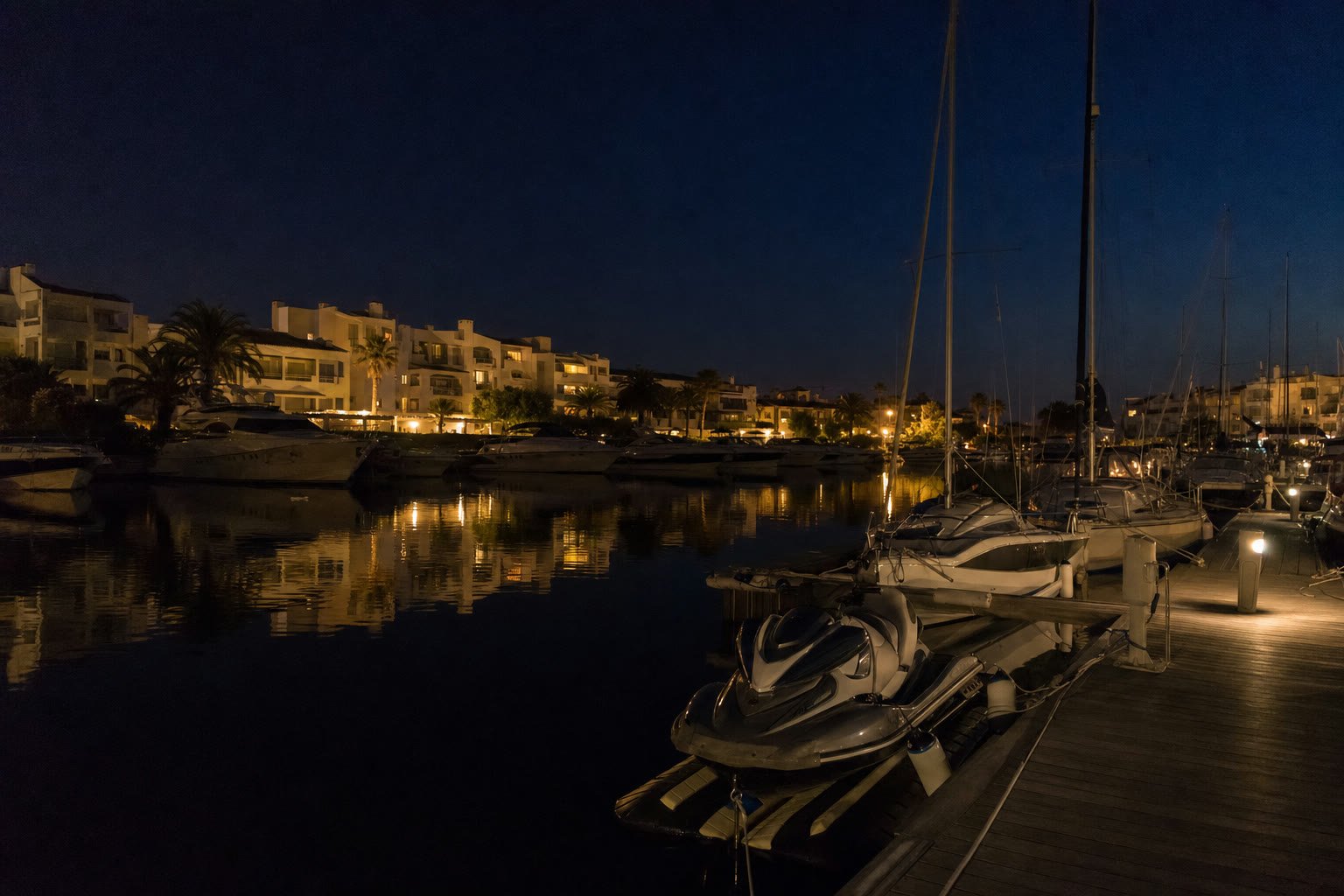 Darses d'un port de plaisance résidentiel méditerranéen de nuit, jet-ski amarré au ponton, terrasses encore éclairées